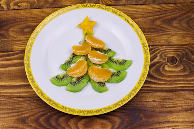 Árvore de Natal feita de fatias de kiwi e lóbulos de tangerina na mesa de madeira. Vista do topo. Ideia criativa para sobremesas festivas de Natal e Ano Novo. Ideia divertida de comida para crianças