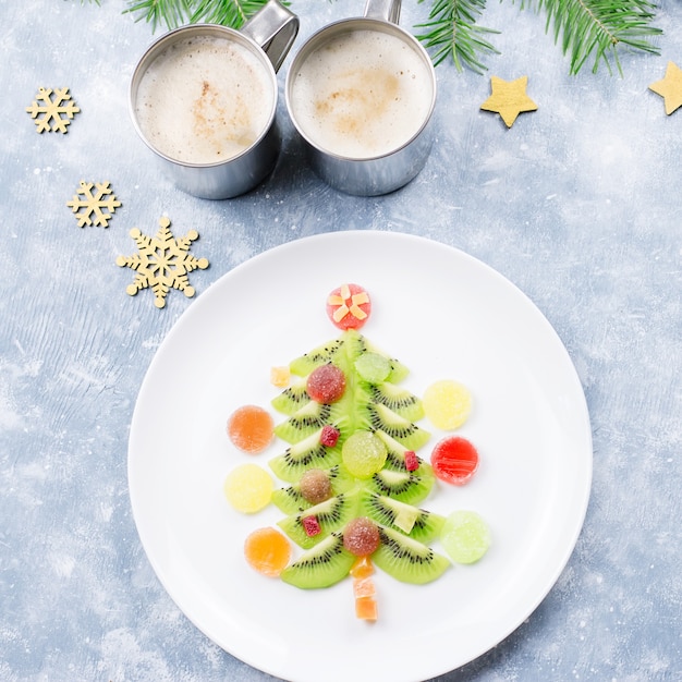 Árvore de Natal feita de kiwi e geleia de frutas em um prato com galhos de pinheiro e enfeites. Vista superior, copie o espaço