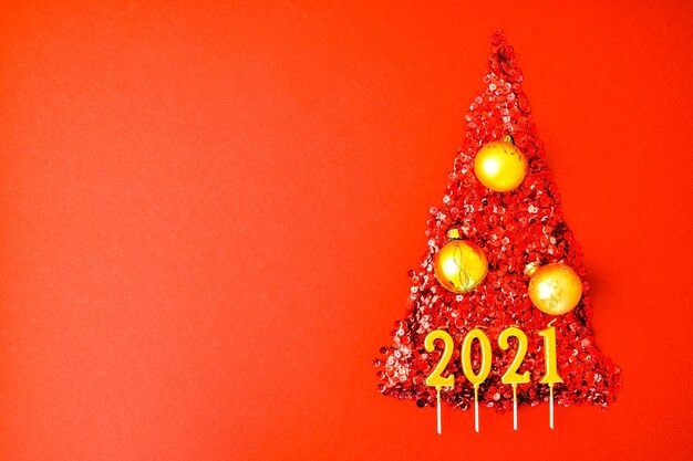 Árvore de Natal feita por confete brilhante sobre fundo vermelho. Velas de ouro de 2021 anos. Cartão de ano novo e feliz Natal. Conceito de férias