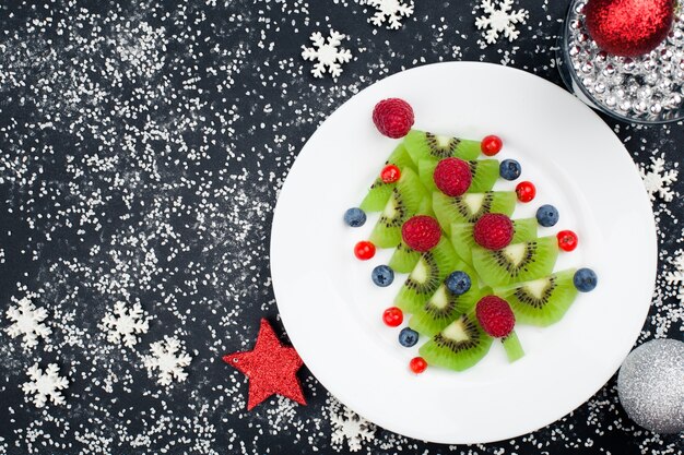 Árvore de natal kiwi com framboesa, mirtilo e amora na mesa com decoração