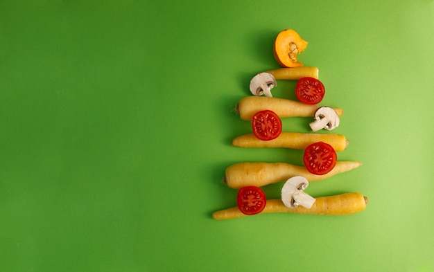 Árvore de Natal montada a partir de legumes, tomates, cenouras, cogumelos em uma vista superior de fundo verde