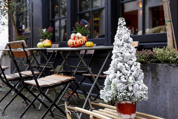 Árvore de Natal na neve no café de rua. Ano novo e Natal em estilo retro vintage europeu, perto de mesas ao ar livre com cadeiras no terraço do café. Comida de rua da Feira de Natal.