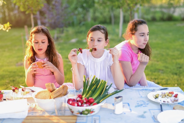 Árvore meninas bonitos sentado junto à mesa na natureza e almoçar.