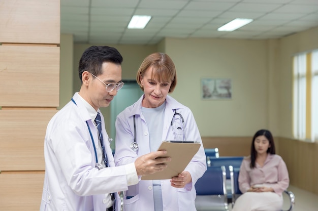 Ärzte aus Asien und dem Westen halten ein Tablet in der Hand und unterhalten sich über einen Patienten in einem Krankenhaus.