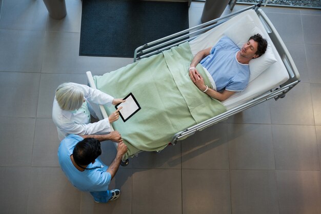 Ärzte diskutieren über digitale Tablette im Korridor, während Patient auf Notfalltrage liegt