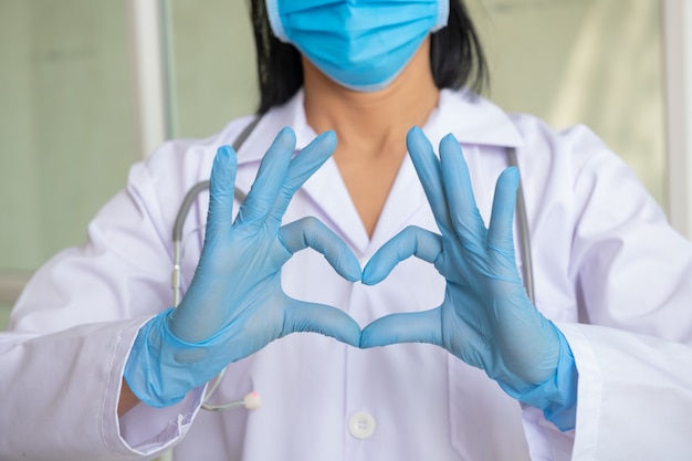 Ärzte, Infektionsmediziner, Forscher und Covid 19-Konzept. Frau mit medizinischer Maske und Händen im Latexhandschuh zeigt das Symbol des Herzens. Doktor für das Herz. Liebe zu deiner Bauchspeicheldrüse. medizinische Fachkräfte