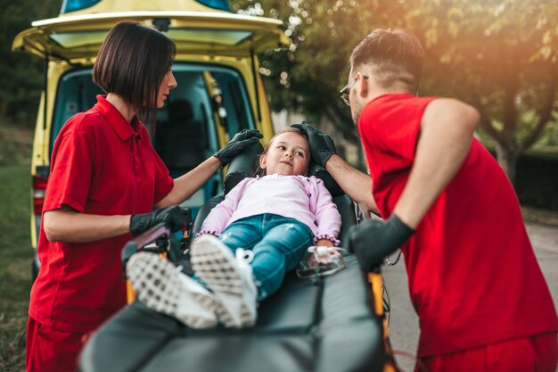 Ärzte mit verletztem kleinen Mädchen vor Krankenwagen.