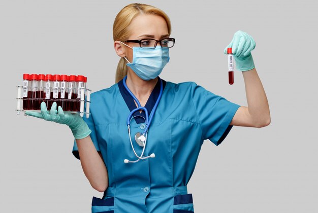 Ärztin der Krankenschwester der Schutzmaske und der Handschuhe, die Gestell mit Virusbluttests halten