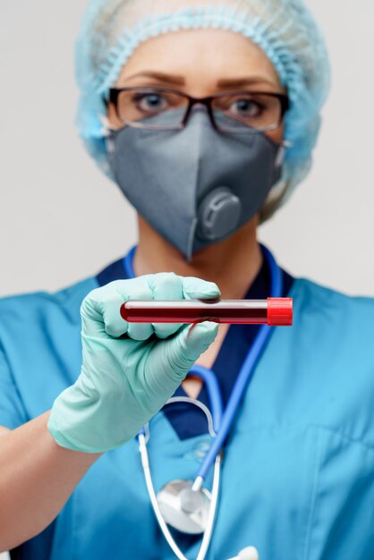 Ärztin der Krankenschwester, die Schutzmaske und Handschuhe trägt und Virusblut-Reagenzglas hält