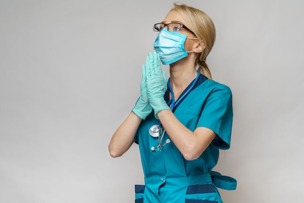 Ärztin der Krankenschwester, die Schutzmaske und Latexhandschuhe trägt - betend und hoffnungsvolle Geste