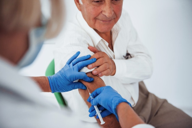 Ärztin, die älteren männlichen Patienten mit Spritze in der Klinik injiziert.