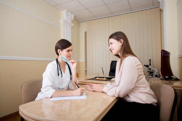 Ärztin, die am Schreibtisch im Büro sitzt und dem Patienten eine Verordnung schreibt.