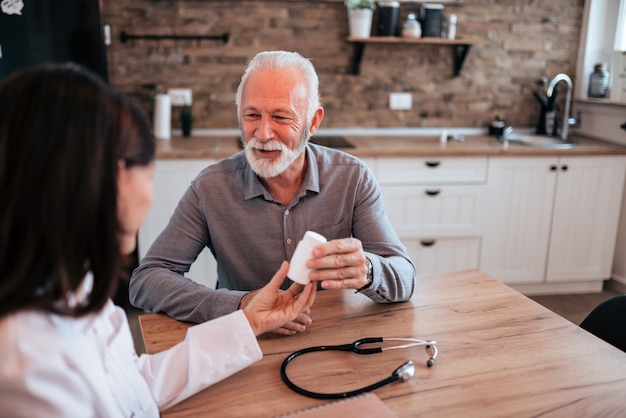 Ärztin, die ein Tablettenfläschchen bei der Unterhaltung mit einem älteren Patienten hält.