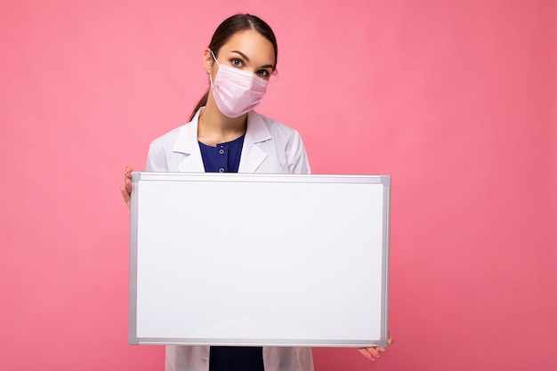 Ärztin, die einen weißen medizinischen Mantel und eine Maske hält, die leere Tafel hält