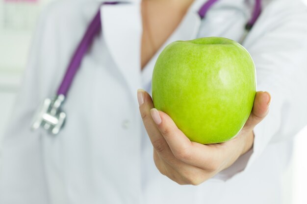 Ärztin, die frischen grünen Apfel hält. Gesundheitswesen und medizinisches Konzept.