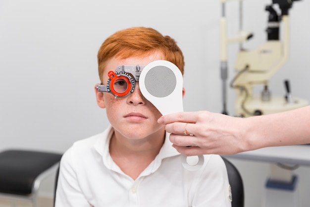 Ärztin, die Sehvermögen des Sommersprossejungen mit Optometrikerversuchsrahmen in der Klinik überprüft