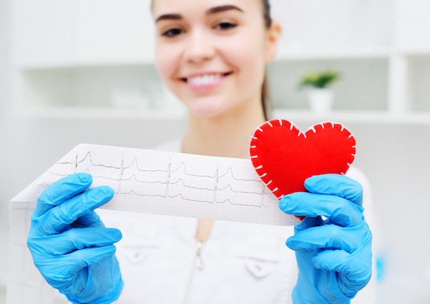 Ärztin hält ein rotes Herz und einen Papierausdruck eines Kardiogramms. Prävention von Herz-Kreislauf-Erkrankungen.