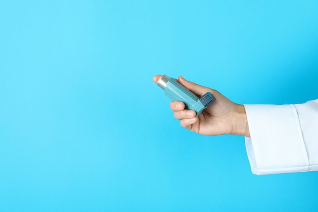Ärztin Hand hält Asthma-Inhalator auf blauem Hintergrund