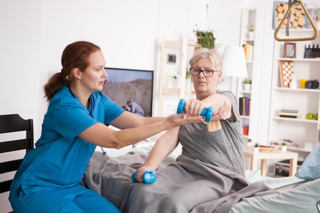 Ärztin hilft älteren Frauen mit Physiotherapie im Pflegeheim mit Hanteln.