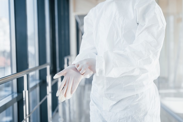 Ärztin im Laborkittel, Schutzbrille und Maske, die drinnen stehen und Handschuhe tragen
