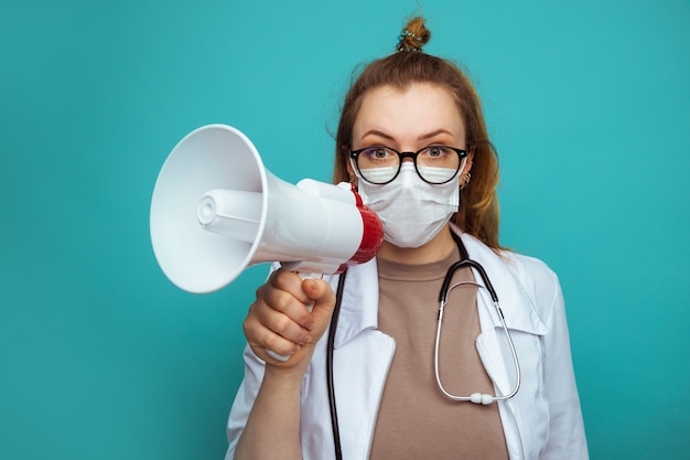 Ärztin im Schutzanzug und Brille mit Maske hält Megaphon.