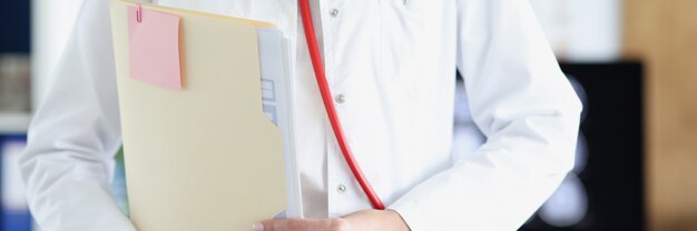 Ärztin im weißen Kittel und Stethoskop hält medizinische Dokumente in der Hand