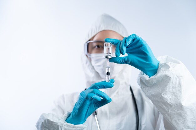 Ärztin in PSA (persönliche Schutzausrüstung), Handschuhen, Gesichtsmaske und Schutzbrille mit Flasche und Nadel des Coronavirus-Impfstoffs.