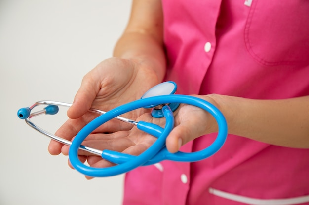 Ärztin in rosa medizinischer Uniform hält Stethoskop in ihren Händen. Lebens- und Krankenversicherung. Berufliche Prüfungen. Medizin und Gesundheit. Gesunder Lebensstil. Moderne Medizin. Medizinische Versorgung.