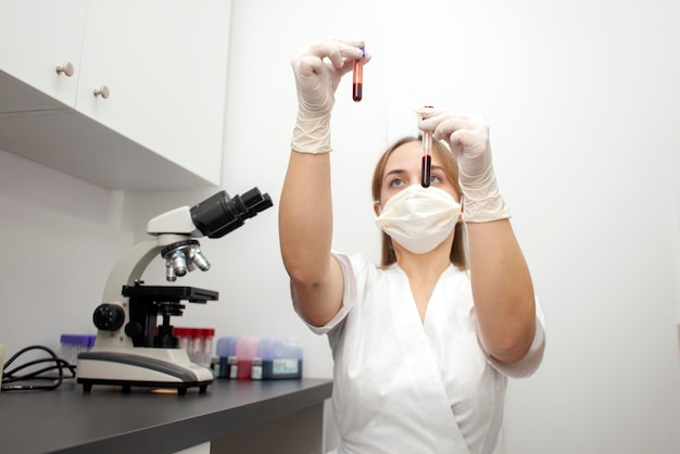 Ärztin in Uniform und medizinischer Maske hält Reagenzgläser mit Blutuntersuchungen im Labor