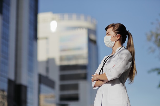 Ärztin, Krankenschwester, die eine schützende Gesichtsmaske in der Stadt trägt. Wolkenkratzer, Himmel