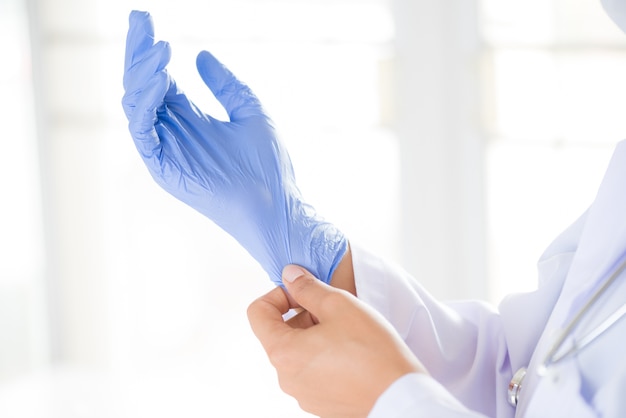 Ärztin mit einem Stethoskop auf einer Schulter, die auf sterile Handschuhe sich setzt.