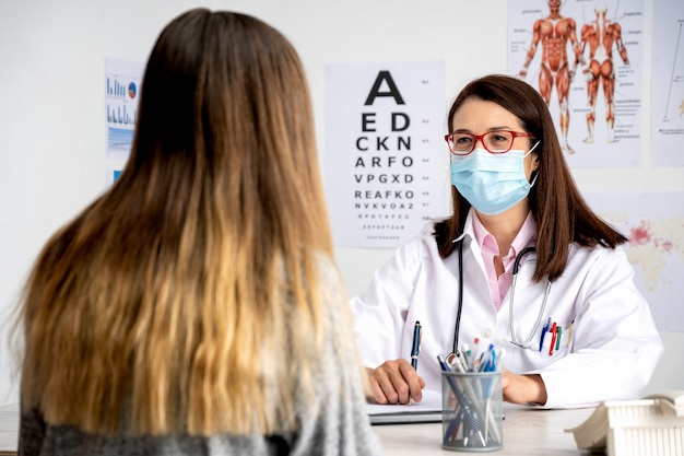 Ärztin mit Maske, die sich um einen Patienten in ihrem Büro kümmert