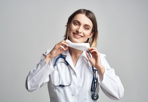 Ärztin mit medizinischer Maske hält Hände in der Nähe des Gesichts, blaues Stethoskop, ausgeschnittene Ansicht