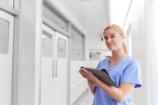 Ärztin mit Scrubs im Krankenhauskorridor mit digitalem Tablet