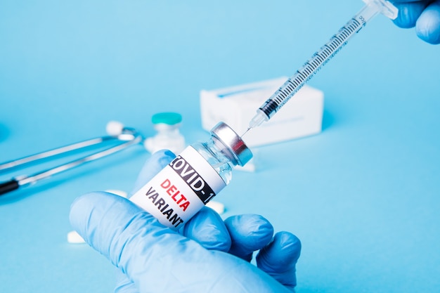 Ärztin mit Spritze und COVID-19-Delta-Varianten-Impfstoff isoliert auf blauem Hintergrund. Gesundheitswesen und medizinisches Konzept.
