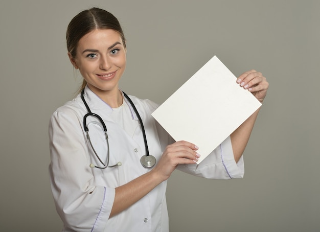 Ärztin mit weißer Liste, stehend auf grauem Hintergrund