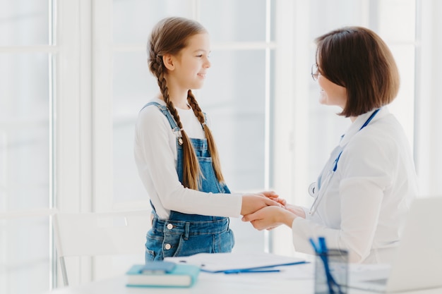 Ärztin schüttelt Mädchen-Patientin die Hand, spricht unterstützende Worte