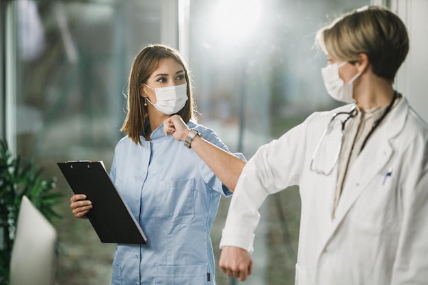 Ärztin und junge Krankenschwester grüßen während der Corona-Virus-Pandemie mit stoßenden Ellbogen im Krankenhaus, um Handshakes zu vermeiden.