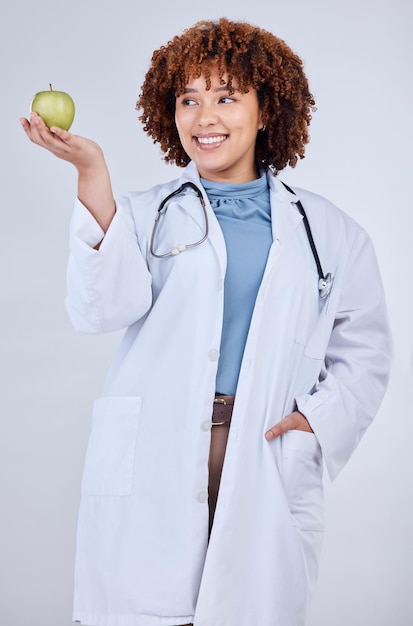 Ärztin und Lächeln mit Apfel im Studio, weißer Hintergrund und Wellness. Glückliche medizinische Mitarbeiterin, Ernährungsberaterin und hält grüne Früchte für Vitamin-C-Ernährung, gesunde Ernährung und vegane Ernährung