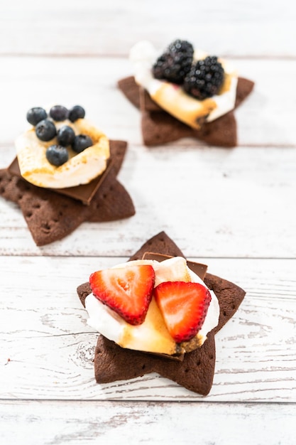 S'mores auf einem hausgemachten sternförmigen Schokoladen-Graham-Cracker mit gerösteten Marshmallows und Früchten zubereiten.