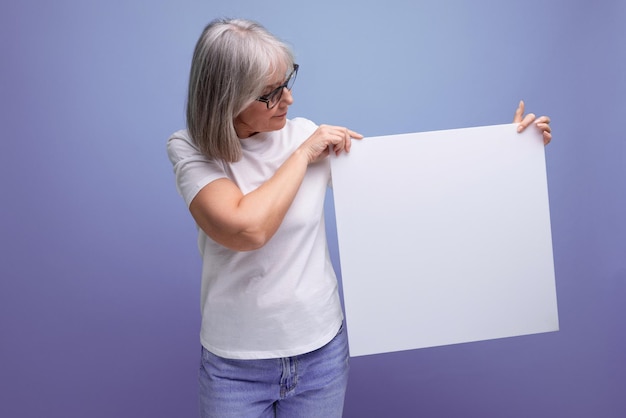 S senhora de negócios madura com cabelos grisalhos segurando folha em branco com mocap para cartaz no fundo do estúdio