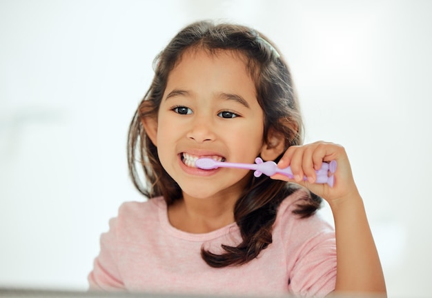 Sabe cepillarse bien. Una foto de una niña adorable cepillándose los dientes en un baño en casa.