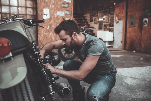 Foto sabe todo sobre bicicletas. hombre joven confidente que repara la motocicleta cerca de su garaje