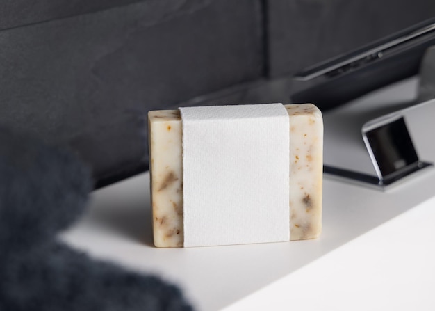 Sabón beige con etiqueta en blanco en el lavabo cerca del grifo y toalla de baño gris oscuro