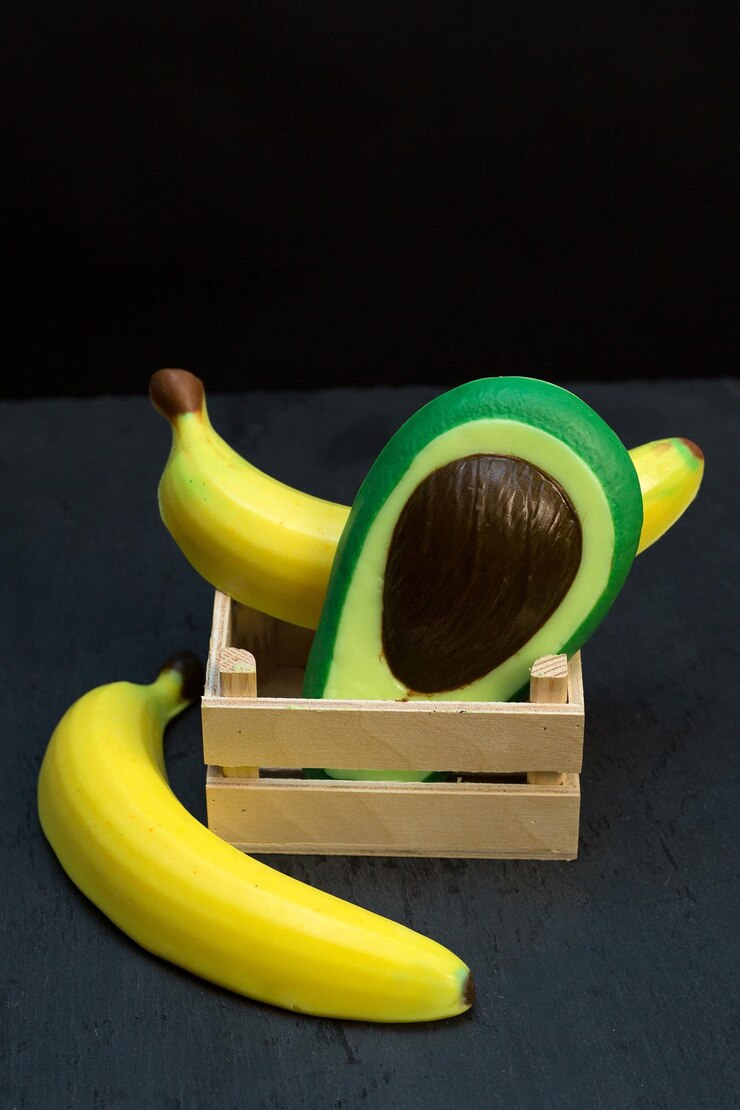 Foto sabón hecho a mano en forma de frutas tropicales aguacates y plátanos en caja de madera de fondo negro