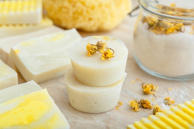 Sabonete branco em barra redonda com ervas secas de flores de calêndula. Os produtos de banho de spa têm aroma de sal, muitos sabonetes artesanais naturais na mesa de mármore. Sólidos shampoo, barra de beleza, cosméticos, spa, produtos de bem-estar.