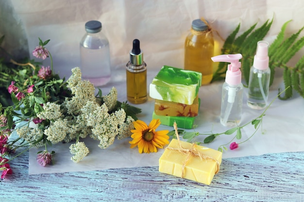 Sabonete, spray, buquê de ervas medicinais e frascos de vidro com óleo aromático em uma mesa de madeira