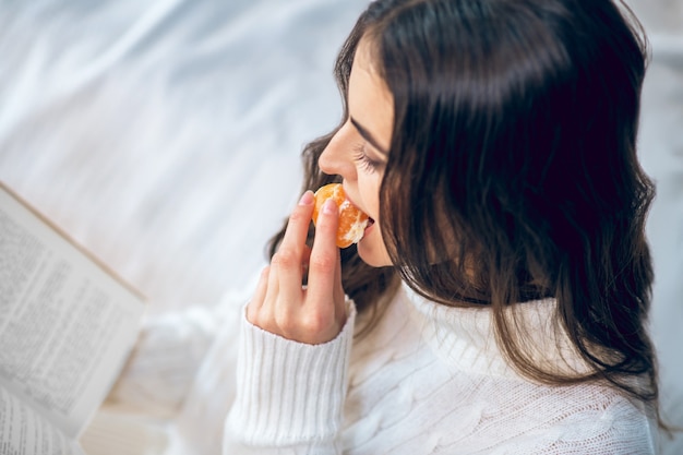 Sabor cítrico. Mujer hermosa joven comiendo mandarina y mirando contento