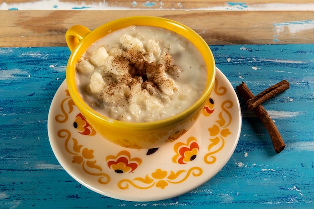 Foto sabor doce típico do brasil canjica porro de milho branco com canela e coco consumido em festivais de junho festa junina em uma mesa azul rústica