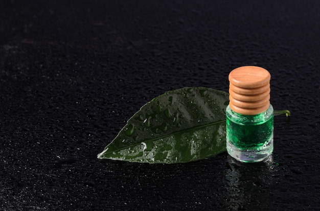 Sabor limón de color esmeralda en frasco de vidrio con tapón de madera sobre una hoja verde con gotitas de agua. La llave oscura.